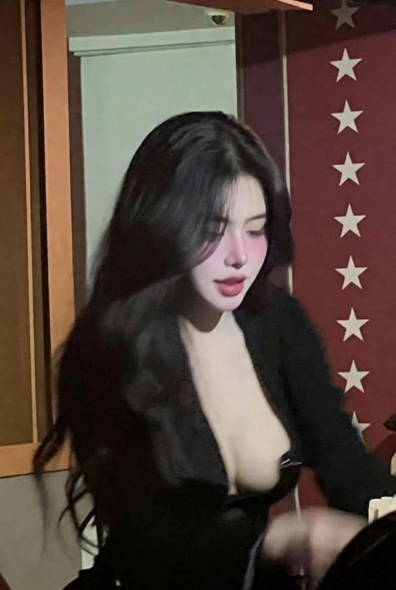 A low-quality iPhone photo of a Vietnamese idol woman in a dimly lit karaoke parlor.